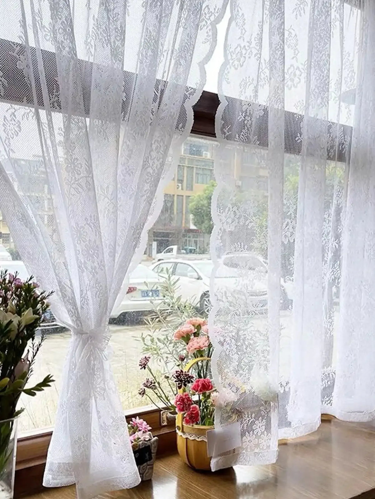 White floral embroidery sheer curtain hanging in a window with blurred outdoor view