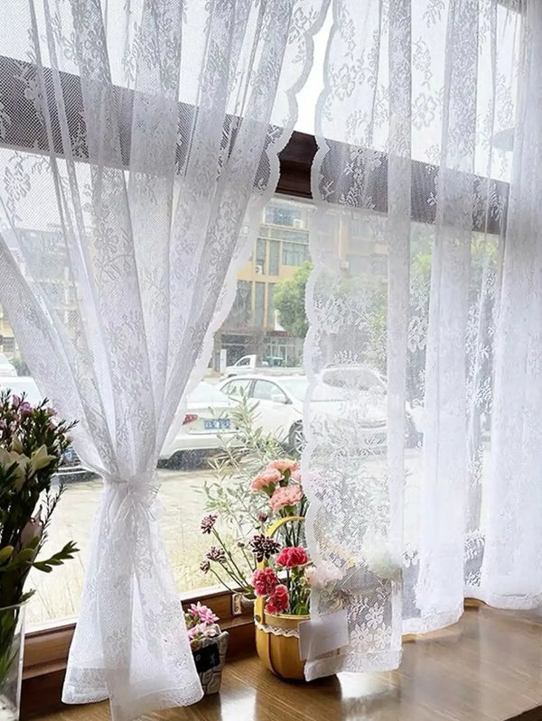 White floral embroidery sheer curtain hanging in a window with blurred outdoor view