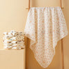 A white baby swaddle blanket with a floral pattern is hanging on a wooden rack.