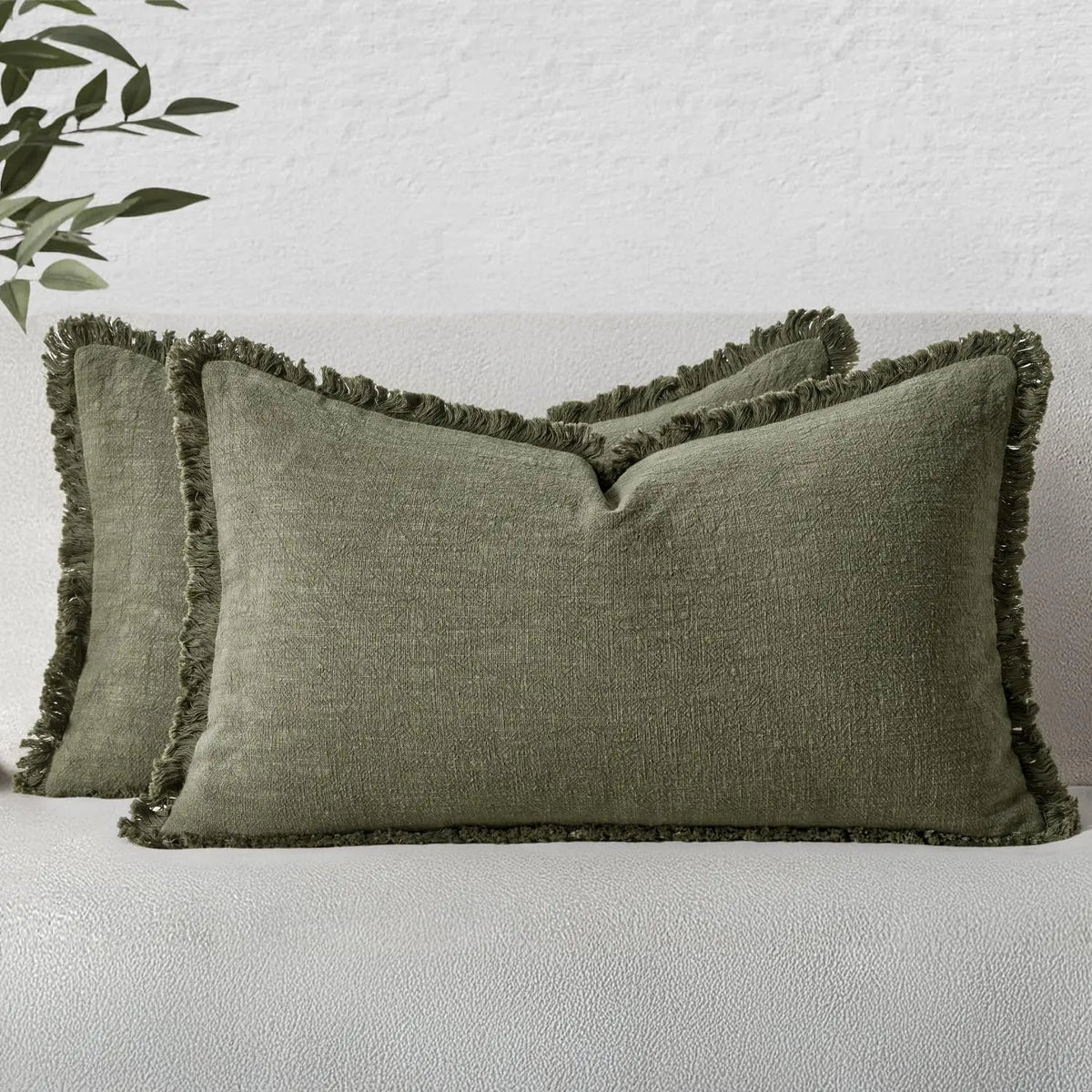 A pair of olive green linen fringe throw pillow covers resting on a light gray sofa.