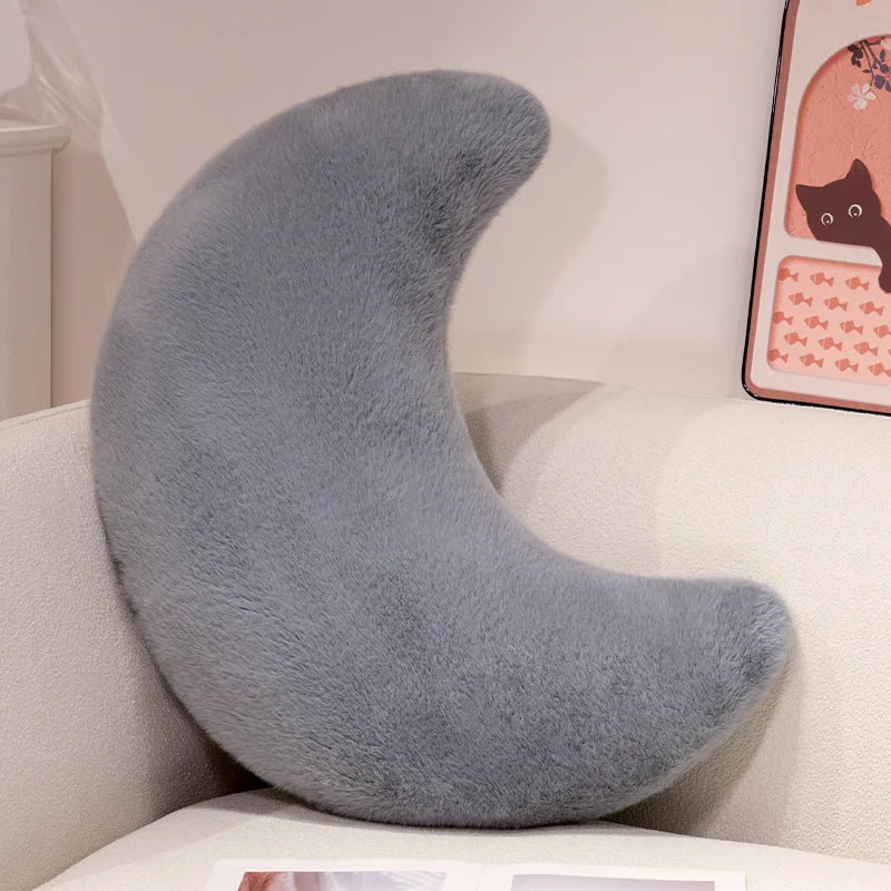 A soft gray moon-shaped throw pillow resting on a white surface.