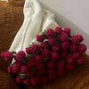 A bouquet of handmade rose crochet flowers in shades of red and green displayed next to a white knitted blanket.