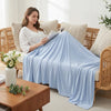 A woman is relaxing on a wicker sofa covered with a light blue ice silk cooling blanket.