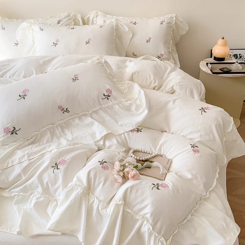 White duvet cover set with pink embroidered roses and ruffled edges on a bed.