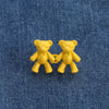 Two yellow bear button pins are displayed on a blue denim fabric.