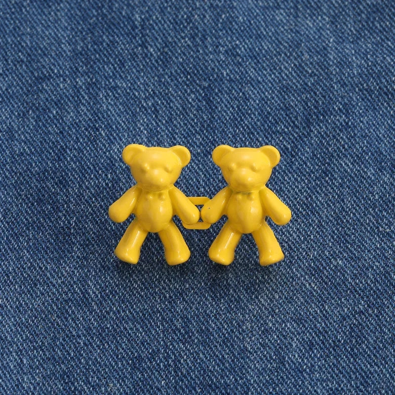 Two yellow bear button pins are displayed on a blue denim fabric.