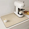 A white espresso machine is placed on a beige kitchen drain mat with coffee cups and toast visible.