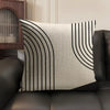 A beige cushion cover with black geometric lines in a vertical pattern resting on a dark leather sofa.