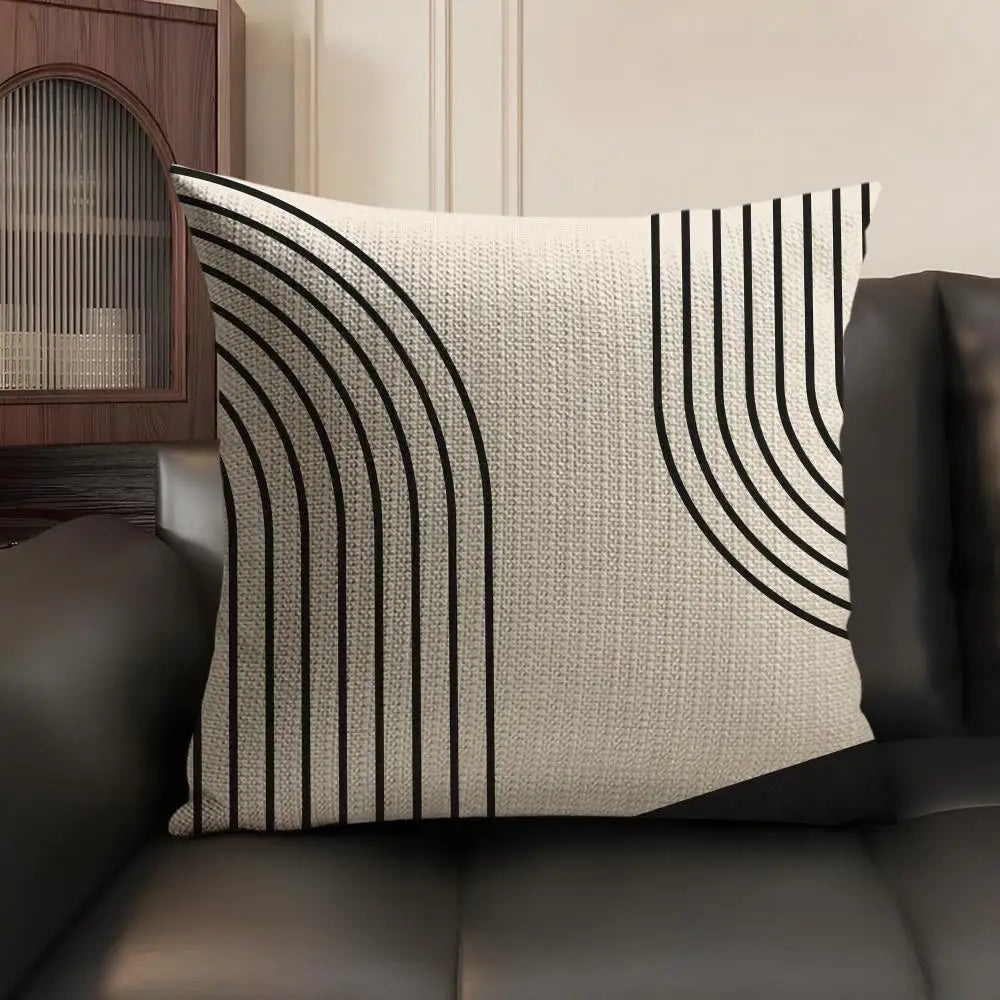 A beige cushion cover with black geometric lines in a vertical pattern resting on a dark leather sofa.