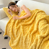 A woman relaxing on a sofa wrapped in a bright yellow ultra-soft coral fleece blanket.