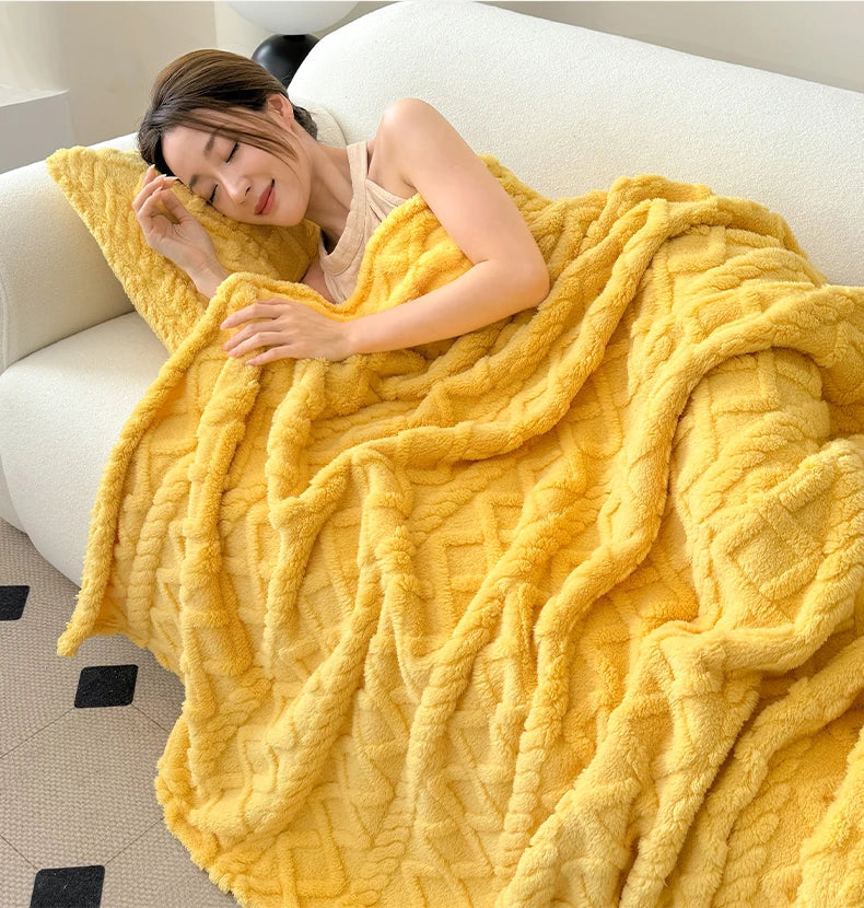 A woman relaxing on a sofa wrapped in a bright yellow ultra-soft coral fleece blanket.