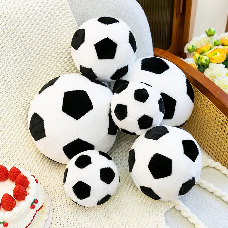 A collection of white and black football plush toys resting on a light-colored textured surface.