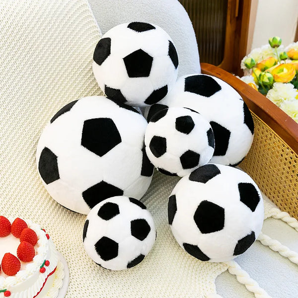 A collection of white and black football plush toys resting on a light-colored textured surface.