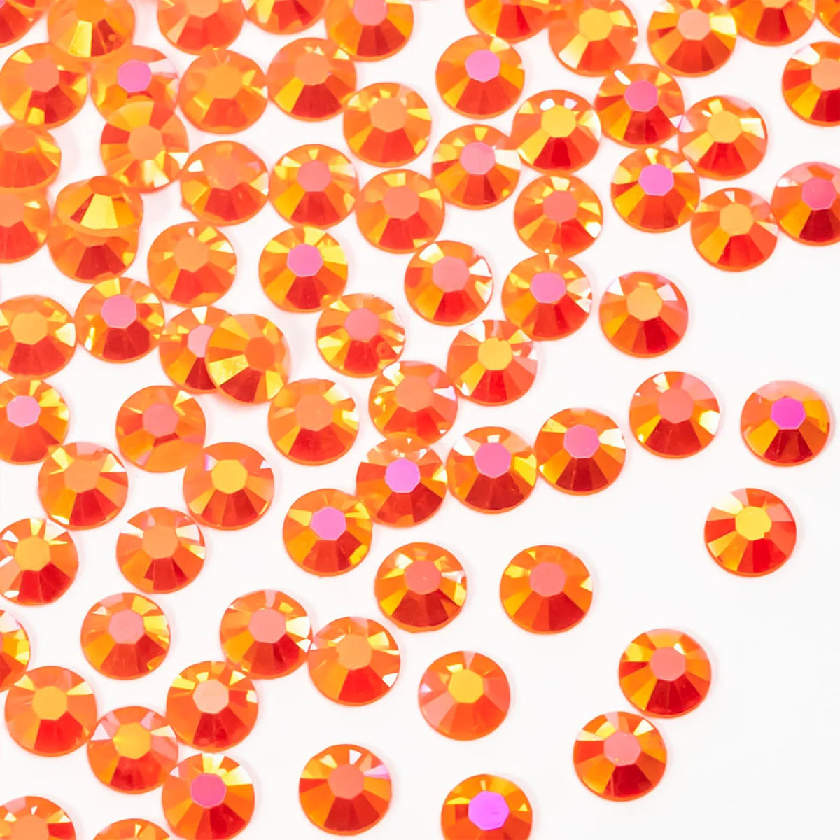 A close-up of small orange-red AB resin flatback rhinestones scattered on a white background.