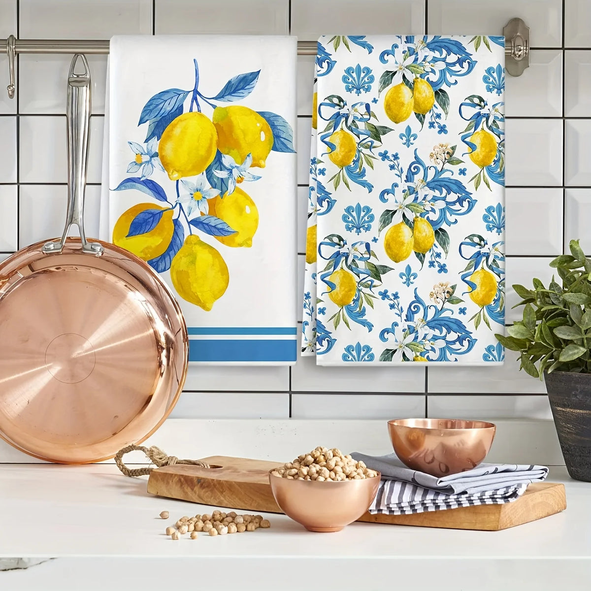 A set of two blue-edged lemon kitchen towels featuring yellow lemons and blue foliage, displayed next to a copper plate and b
