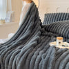 A dark gray faux fur blanket is draped over a bed, emphasizing its soft texture and warmth.