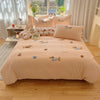 A light peach embroidered bedding set featuring small animal motifs on a bed with sheer curtains.