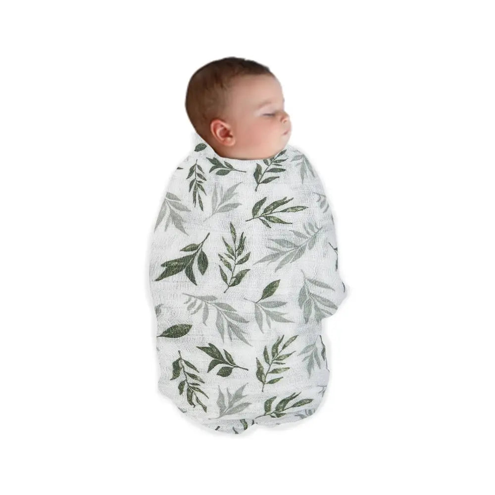 A newborn baby is swaddled in a premium cotton muslin blanket featuring a green leaf pattern.