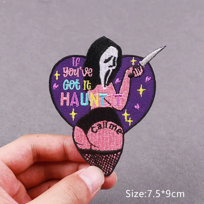 A hand holds an embroidered horror movie patch featuring a ghostly figure and purple text on a black background.