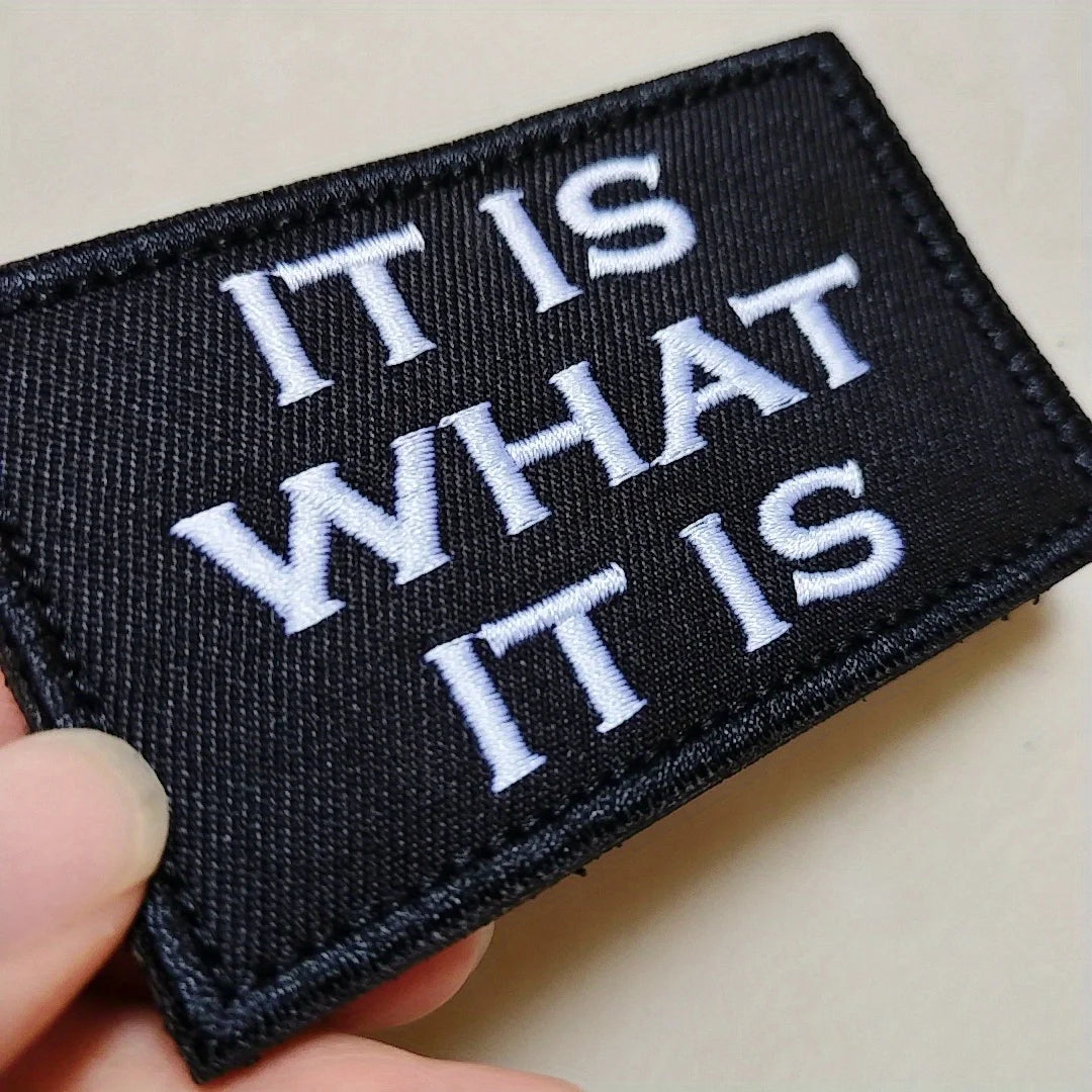 Black embroidered patch with white text reading IT IS WHAT IT IS