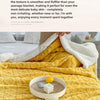 A yellow fleece blanket is shown folded on a bed, with a white blanket draped over it and a lemon resting on the fabric.