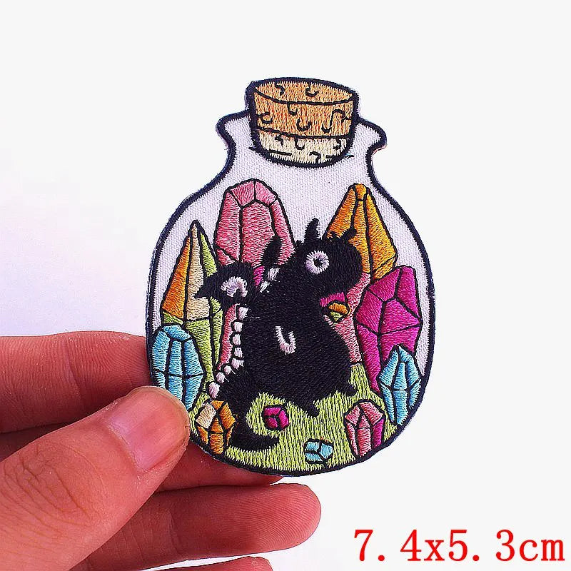 Embroidered iron-on patch featuring a black cartoon cat surrounded by colorful gemstone shapes on a fabric background