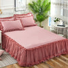 Pink lace bed skirt set with ruffled fabric and pink pillows on a bed.