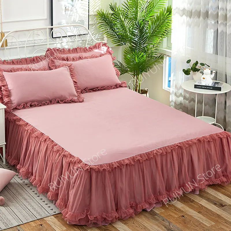 Pink lace bed skirt set with ruffled fabric and pink pillows on a bed.