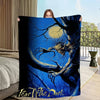 A person holds up a dark blue and black graphic blanket featuring a menacing, skeletal hand against a bright blue background.