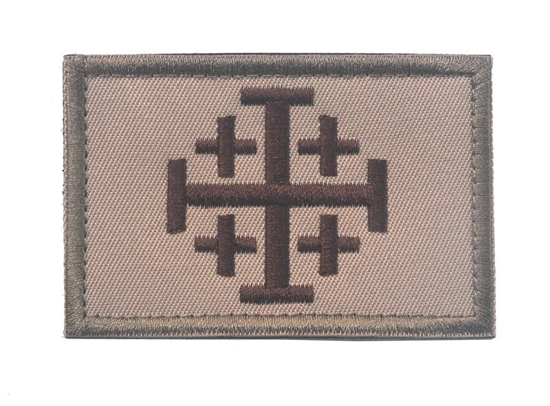 A rectangular embroidered military cross shield patch in tan fabric with a dark brown cross design.