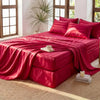 A vibrant red satin bedding set featuring a headboard and pillows on a bed with large windows.
