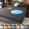 A waterproof mattress protector sheet is shown being used on a dark gray bed, with blue water dripping onto the surface.