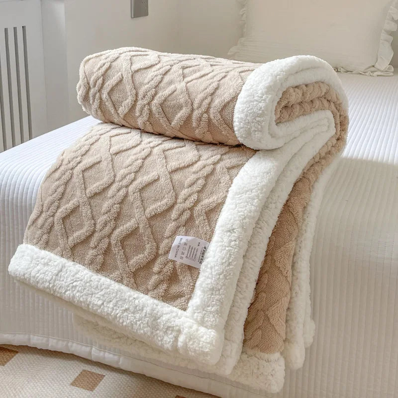 A thick fleece blanket in beige and white diamond pattern is folded on a white bed.
