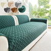A dark green quilted sofa cushion with a white trim and a light beige floor covering.