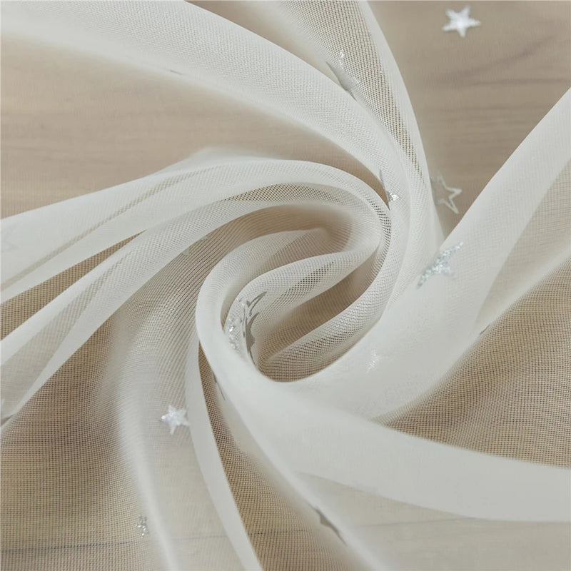 Flowing beige tulle fabric with silver star embellishments creating a soft swirl.