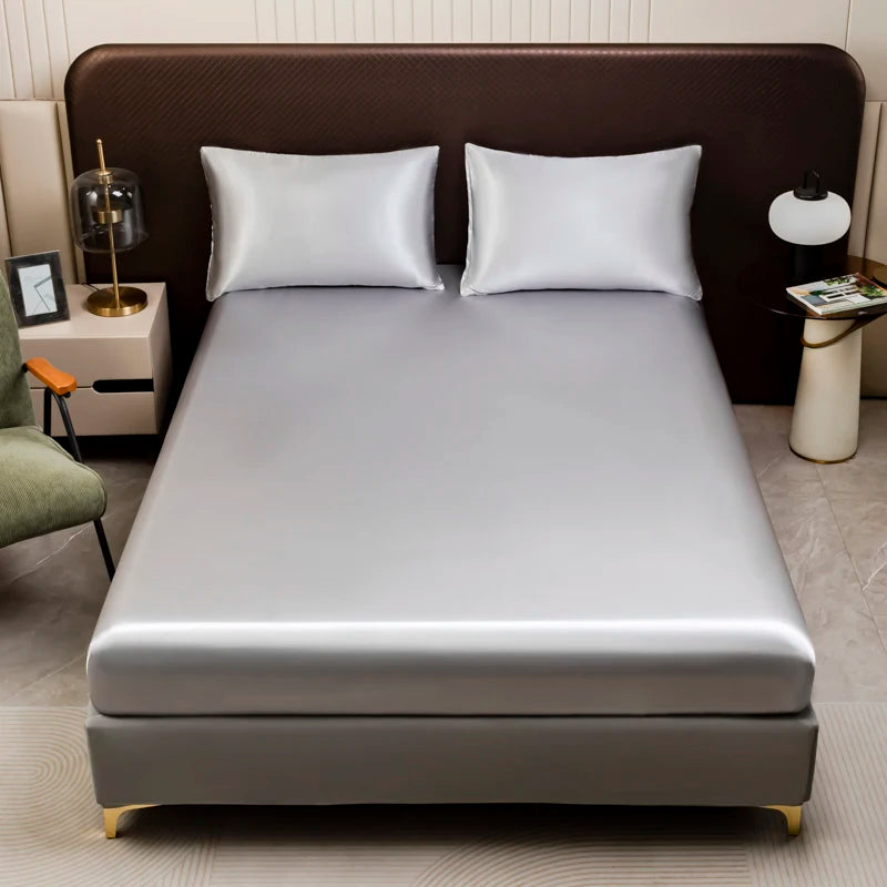 A silver satin bedding set featuring a fitted sheet and two white pillows on a bed.