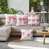 A collection of pink bow pattern decorative pillows displayed on a sofa and a wooden table.