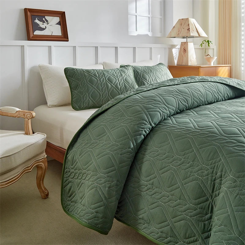 A green quilted duvet and pillows on a bed with white paneling and wooden furniture.