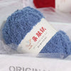 A hand-knitted blue fuzzy yarn ball labeled as Soft Coral Velvet Yarn for Crafting