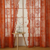 A set of sheer orange floral lace curtains hanging in a window frame.