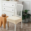 A white wooden dining chair with a beige seat cover is positioned in front of a white dresser and a potted plant.