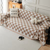 A beige and white checkerboard sofa slipcover draped over a light-colored sofa with a throw pillow and shoes nearby.