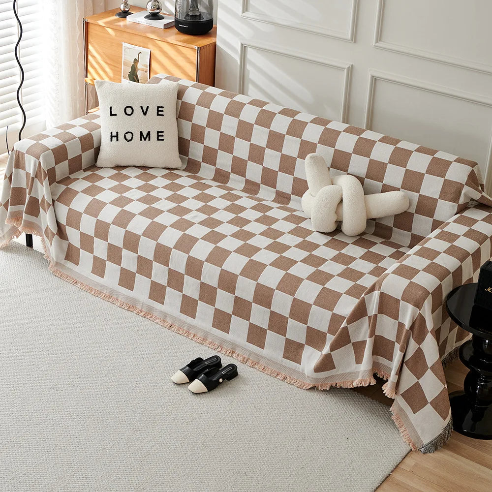 A beige and white checkerboard sofa slipcover draped over a light-colored sofa with a throw pillow and shoes nearby.