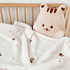 A soft, light beige animal-shaped blanket with brown stripes is draped over a wooden crib railing.
