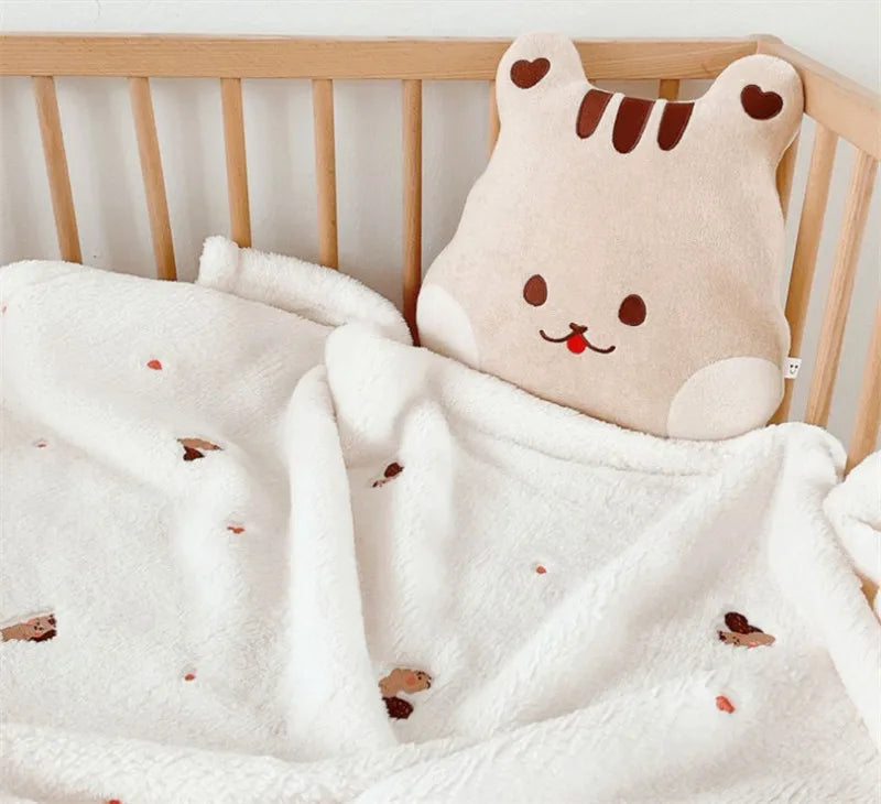 A soft, light beige animal-shaped blanket with brown stripes is draped over a wooden crib railing.