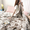 A woman is wrapped in a fluffy gray rabbit fur throw blanket on a bed.