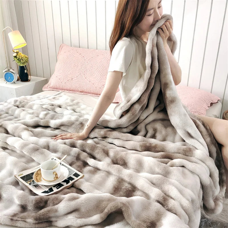 A woman is wrapped in a fluffy gray rabbit fur throw blanket on a bed.