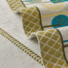 A close-up of a beige fabric with yellow and blue geometric patterns, showing a decorative trim detail.