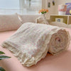 A rolled summer floral print quilt blanket with white lace trim resting on a pink surface.