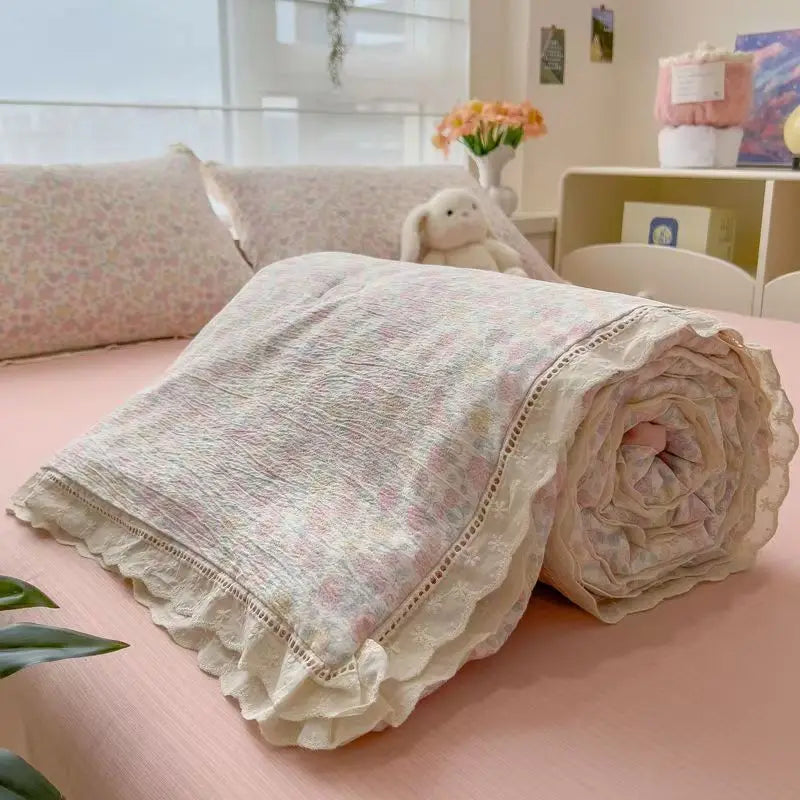 A rolled summer floral print quilt blanket with white lace trim resting on a pink surface.